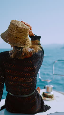 Happy woman relaxing on beard of luxury yacht in summer vacation, back view. Summer holidays in exotic countries, traveling to sea or ocean, bright sun illuminating water surface and white boat