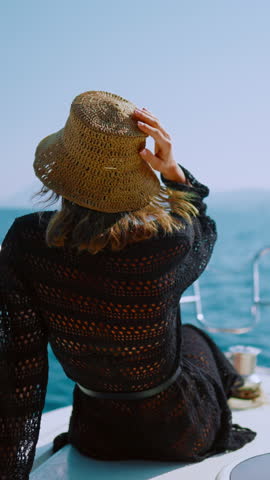 Happy woman relaxing on beard of luxury yacht in summer vacation, back view. Summer holidays in exotic countries, traveling to sea or ocean, bright sun illuminating water surface and white boat