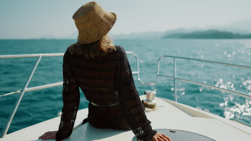 Luxury life and rest in summer vacation, happy lady enjoying yacht trip by sea. Back view of woman sitting on nose of pleasure boat in sunny day, holidays and weekend in ocean, carefree female person