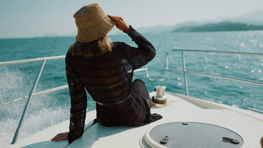 Luxury life and rest in summer vacation, happy lady enjoying yacht trip by sea. Back view of woman sitting on nose of pleasure boat in sunny day, holidays and weekend in ocean, carefree female person
