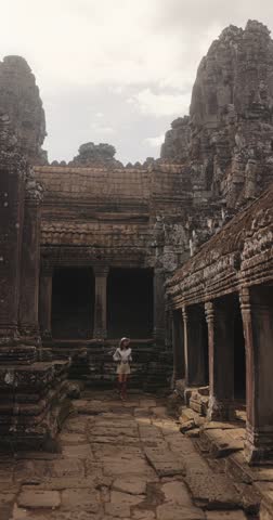 Vertical cinematic footage of a young woman exploring the ancient Bayon Temple in Angkor Thom, Cambodia. High quality stock video concept for adventure, travel, culture, tourism, and history promo.