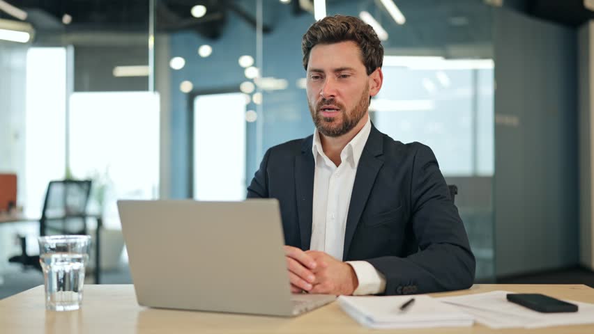 Professional businessman in a suit jacket passionately discussing ideas during a video call in a modern office, showing confidence and engagement.