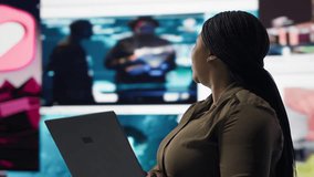 Woman uses laptop, enjoying leisure time with content on video streaming services. African american person watches media VOD broadcasts on notebook in front of digital backdrop with clips, camera B - Powered by Shutterstock - Get 15% off with code: PIKWIZARD15
