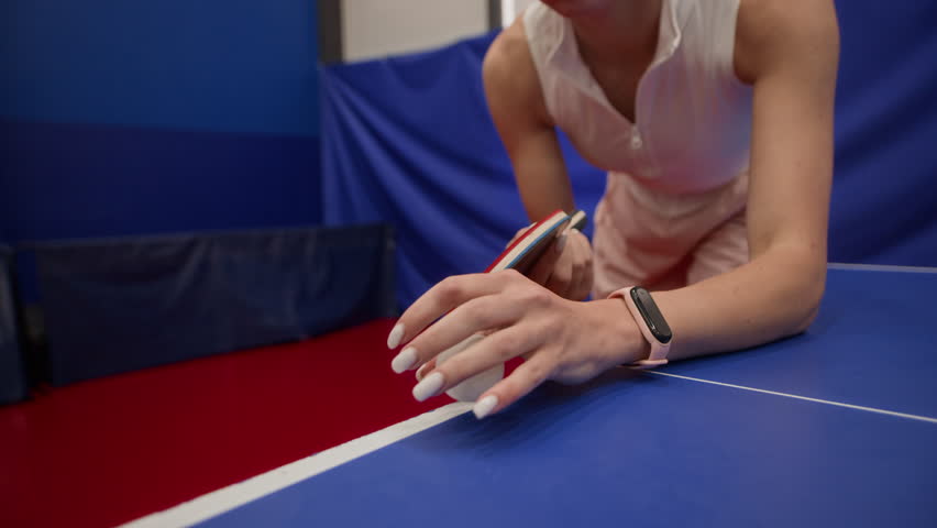 Focused young woman in sportswear tossing ball into air then serving slice shot during table tennis match in gym, slow motion