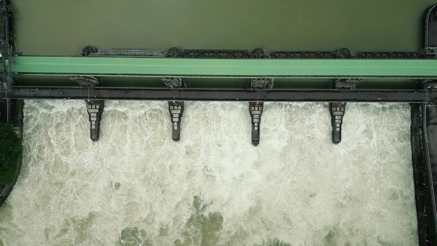 Top view of opened full-flow gates and huge water stream on hydroelectric power station. Aerial view of water dam with cascades of water flowing down