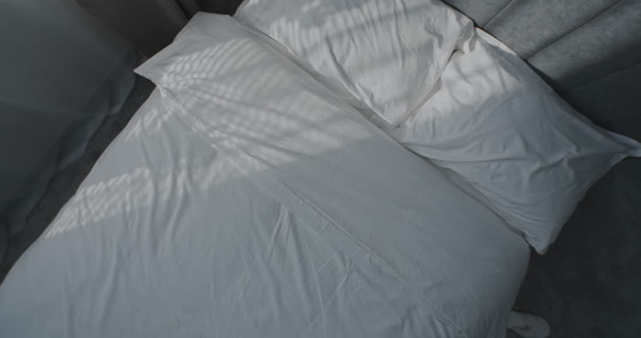 Asian Girl Falls Onto Snow-white Bed with Arms Outstretched, Smiling Happily, Stretching and Basking in Bed. Concept of Relaxation, Comfort, Beautiful Morning, Healthy Lifestyle. Rotating Top View.