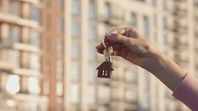 Real estate agency concept, close up of female agent handing home key with house shaped keychain to client in front of modern apartment building. Professional service, property purchase, housing deal. - Powered by Shutterstock - Get 15% off with code: PIKWIZARD15