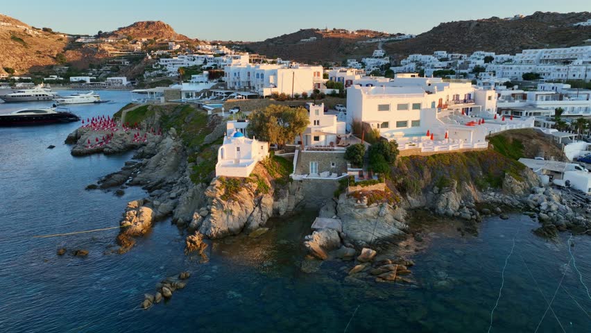 flying above luxury resort on Greek island of Mykonos at sunrise, idyllic Greek harbour with yachts and traditional whitewashed houses, travel on Greek islands. High quality 4k footage