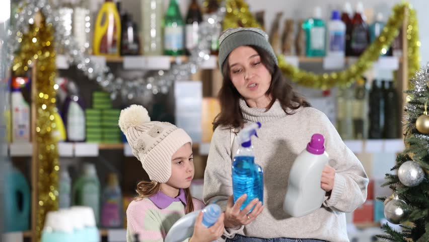 Mother and daughter choose for window cleaning spray and detergent together during Christmas at home improvement store. High quality 4k footage