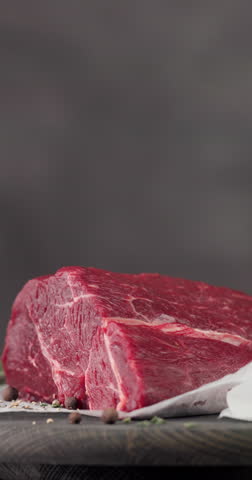 Fresh raw beef meat with pepper and thyme turning on dark wooden cutting board