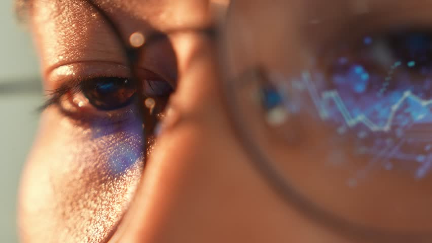 A person wearing glasses uses a laptop, with a digital graph reflected in the glasses, representing data analysis, financial trends, technological progress, and the impact of digital transformation.
