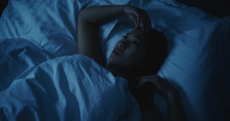 Young Tired Asian Woman With Anxious Thoughts Cannot Sleep at Night. Girl Tries to Lie Down More Comfortably and Fall Asleep. Concept of Stress, Insomnia, Anxious Thoughts, Poor Sleep. Static Shot.