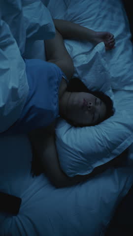 Asian Girl Suffering From Insomnia, Upset and Restless in Bed. She Tosses, Turns, and Struggles to Fall Asleep. Face Showing Stress, Exhaustion. Concept of Poor Rest, Tension, Insomnia. Vertical Shot.