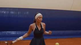 Young female tennis player wearing navy athletic dress returning shots with strong hits during rally practice on red clay court under inflated dome - Powered by Shutterstock - Get 15% off with code: PIKWIZARD15