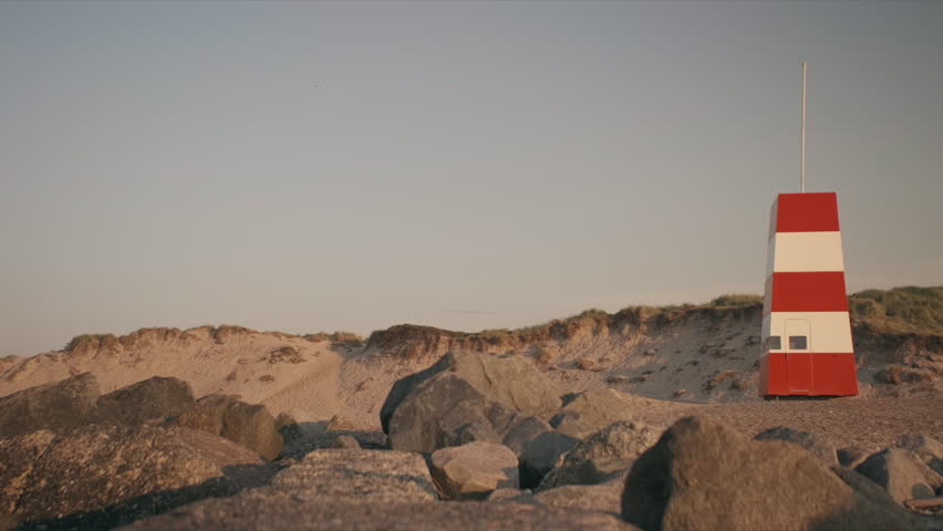 A wide static shot of a lifeguard tower standing tall among coastal rocks on Vorupor's rugged shoreline