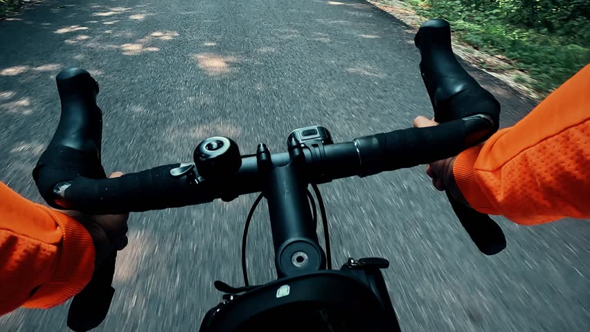 Point of view shot of a cyclist in orange sleeves holding the handlebars of a road bike on asphalt road. Motion blur on the pavement, outdoor sports and training concept