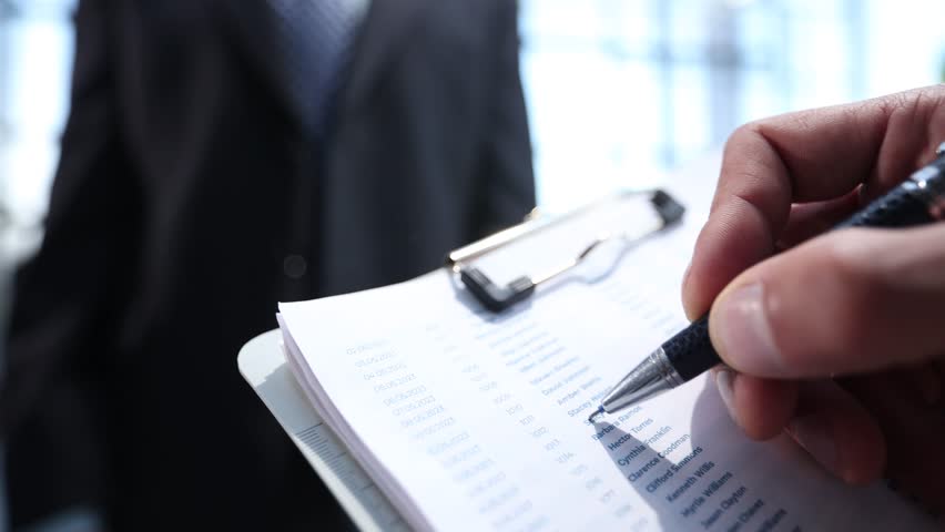 A man is writing on a clipboard with a pen - Powered by Shutterstock - Get 15% off with code: PIKWIZARD15