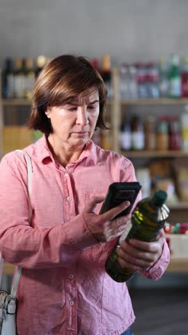 Female buyer checks suitability - scans QR code on olive oil label in a grocery store. High quality 4k footage