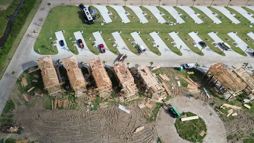 Close-up timber-framed stilt vacation homes under construction in Crystal Beach, Bolivar Peninsula, Texas. Elevated design supports flood resilience, short-term rental use, manmade drainage canal. USA