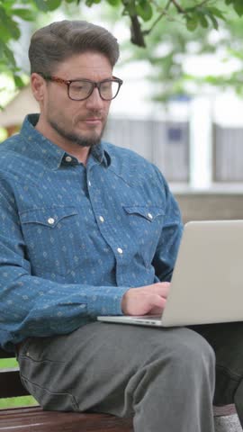 Vertical Video of Cheerful Middle Aged Man with Laptop Enjoying Win on Park Bench
