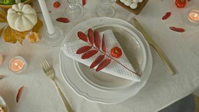 Top down view of branch with red leaves, mini pumpkin and white napkin on plate near fork and knife on festive table set in autumn style for thanksgiving celebration - Powered by Shutterstock - Get 15% off with code: PIKWIZARD15