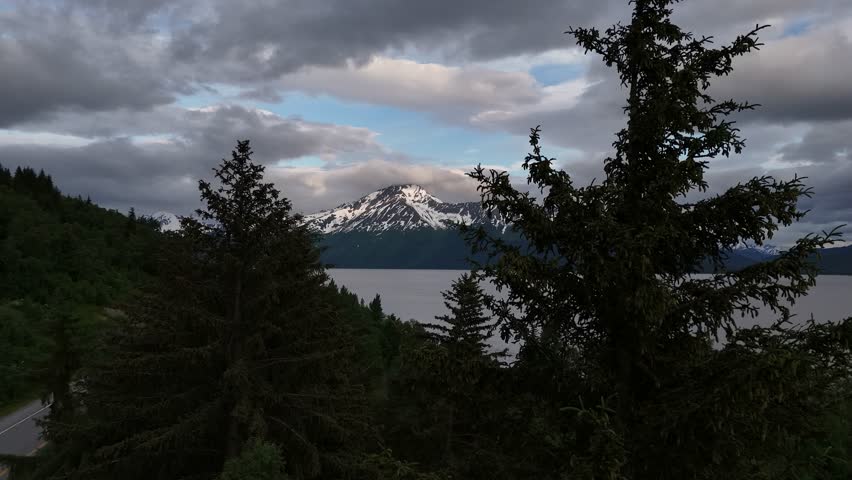 Close up View of Two Pine Trees with Tall Mountain Peak in Background, Mount Alpenglow, Kenai Mountains, Turnagain Arm in Alaska, Late Evening, End of June, Cloudy sky with light patches of blue
