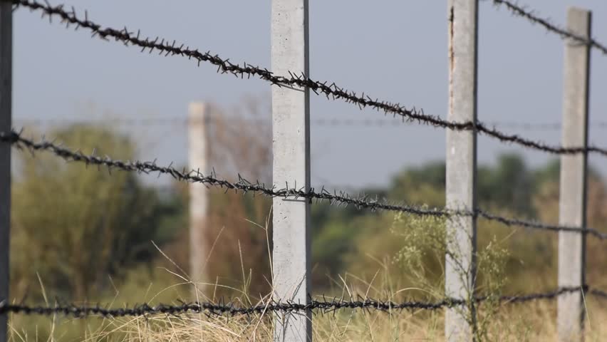 Sunrise behind a barbed wire fence over natural prairie grasslands in Pakistan, A large fence with rows of barbed wire in a field, Concrete pole with wire fencing around rice