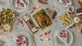 High angle zoom out view of fall table setting displaying baked turkey, appetizers, salad, baby potatoes, plates with napkins and red leaves, decorative pumpkins and lit candles - Powered by Shutterstock - Get 15% off with code: PIKWIZARD15