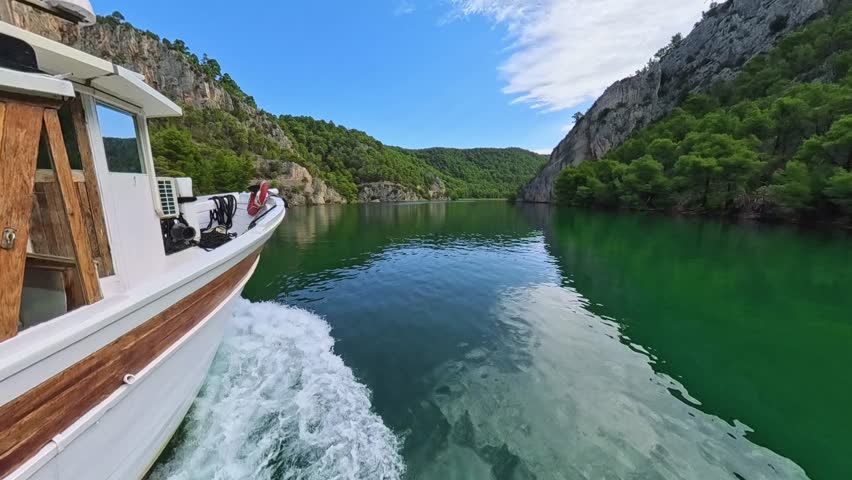 Footage from a moving tourist boat on the calm, green Krka River in Croatia. The view glides through a dramatic gorge with forested slopes on both sides, showcasing the park’s natural beauty.