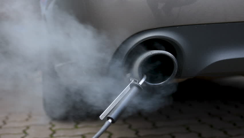 Car exhaust pipe emits dense smoke during emission test on city pavement. Pollution control device measures harmful gases. Service car center garage workshop.  Automobile repair check up diagnosis