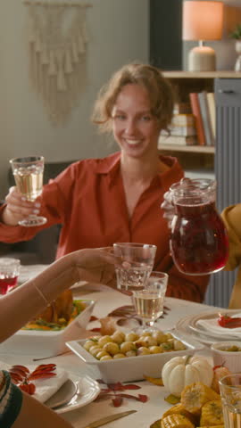 Vertical view of unknown man pouring drink for anonymous woman, then they clinking glasses with smiling girt and another friend while having holiday meal on thanksgiving day