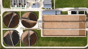 Aerial view of a modern wastewater treatment plant with large circular tanks, filtration pools, and industrial infrastructure. The facility is surrounded by green landscape, showing the contrast - Powered by Shutterstock - Get 15% off with code: PIKWIZARD15