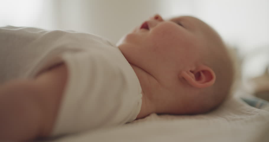 Cute baby boy moving on changing table, smiling at the camera with a thoughtful expression.