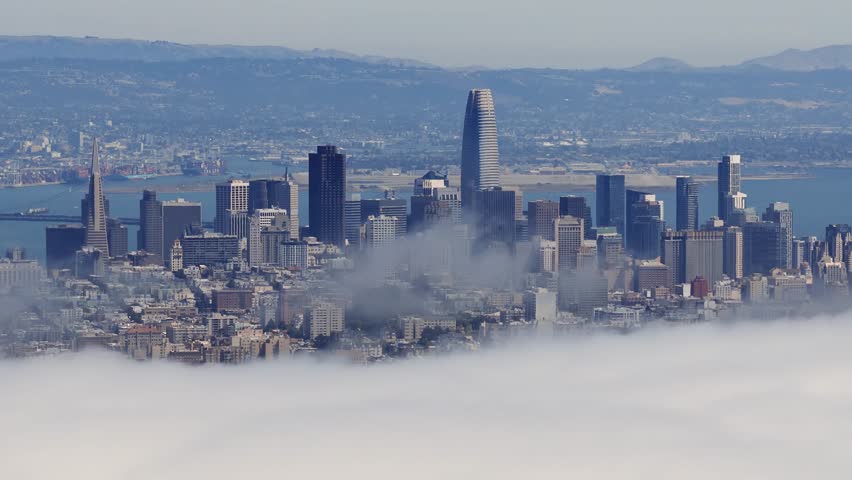 Aerial view of San Francisco skyline featuring Transamerica Pyramid and Salesforce Tower emerging above clouds with motion revealing the cityscape.