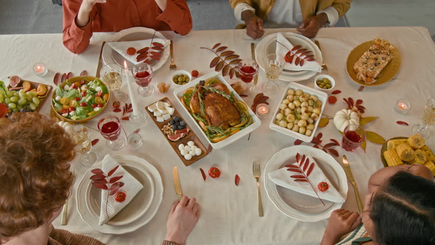 High angle shot of four diverse young friends holding hands and praying before getting down to festive lunch at autumn themed table
