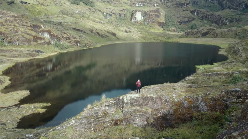 Young traveler with a backpack contemplating the landscape from the top of a mountain overlooking a lagoon. A tourist exploring nature, enjoying freedom and adventure. Healthy lifestyle.