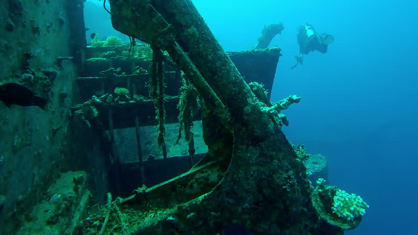 Scuba diver with camera in his hands swims next to the superstructure on wreck of Salem Express ferry, Slow motion of diver swims in blue depths examines at sunken ship