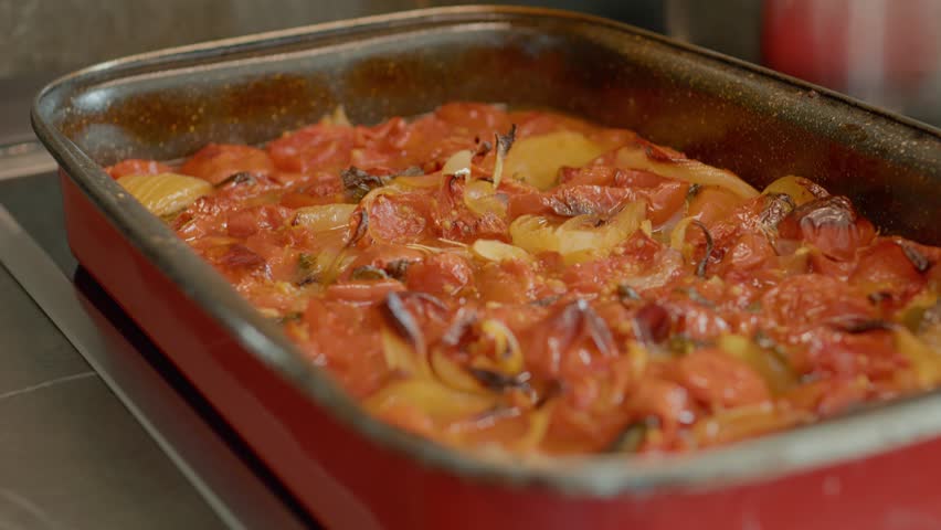 A tray of freshly baked tomatoes, onions, and basil emerges from the oven, showcasing a colorful and healthy dish ideal for any meal. Perfect for serving warm.