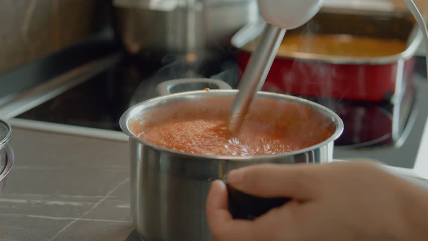 A woman blends fresh tomatoes with onion and basil in a stainless steel saucepan, creating a rich, flavorful tomato sauce perfect for pasta or pizza.