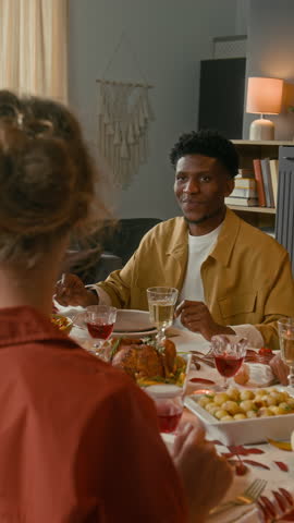 Vertical shot of African American guy chatting with friends and handing plate with vegetable salad to Caucasian girl at festive table