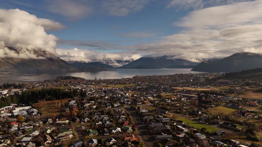 Beautiful aerial view of Wanaka town in New Zealand under a dramatic cloudy sky, capturing lakeside settlement, mountain backdrop and moody atmosphere.