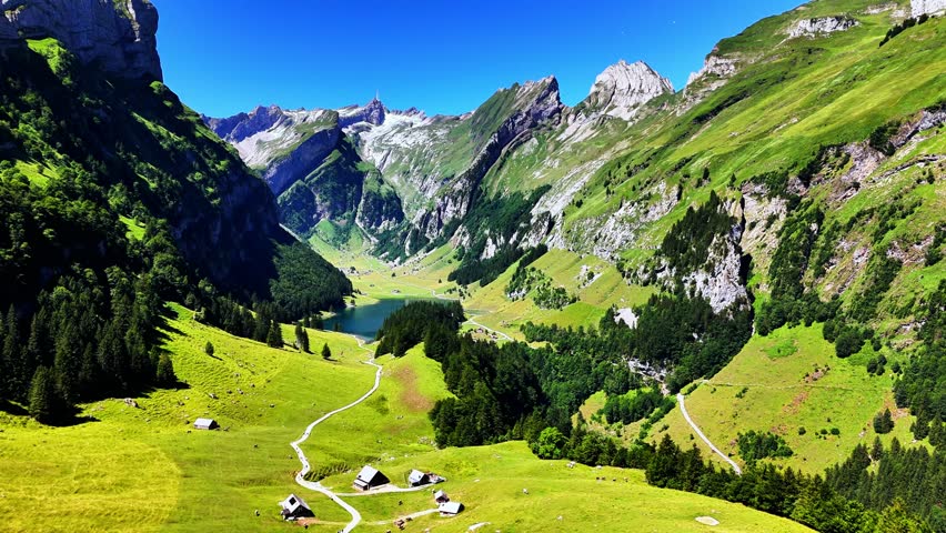 Seealpsee lake nestled in a green Swiss Alps valley with wooden alpine huts, winding trails and clear blue water under sunny skies peaceful, picturesque mountain scenery, Switzerland