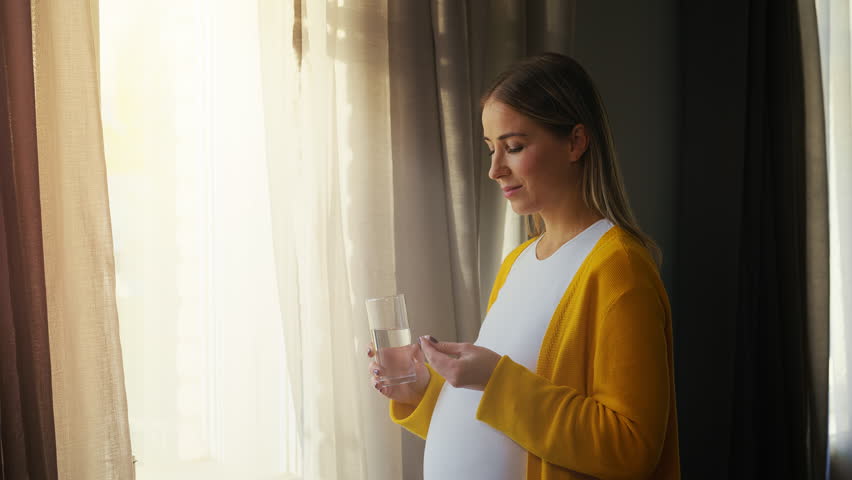 Smiling pregnant woman taking supplement with water, prenatal health care
