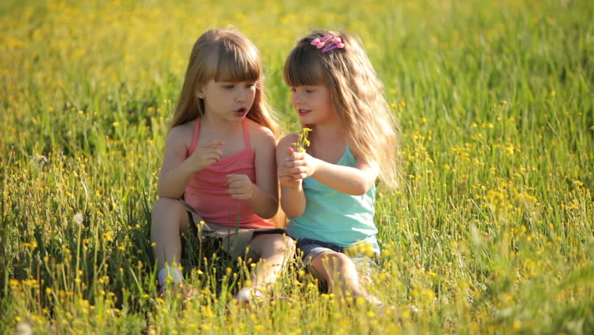 Two little girls sitting on grass and holding flowers

