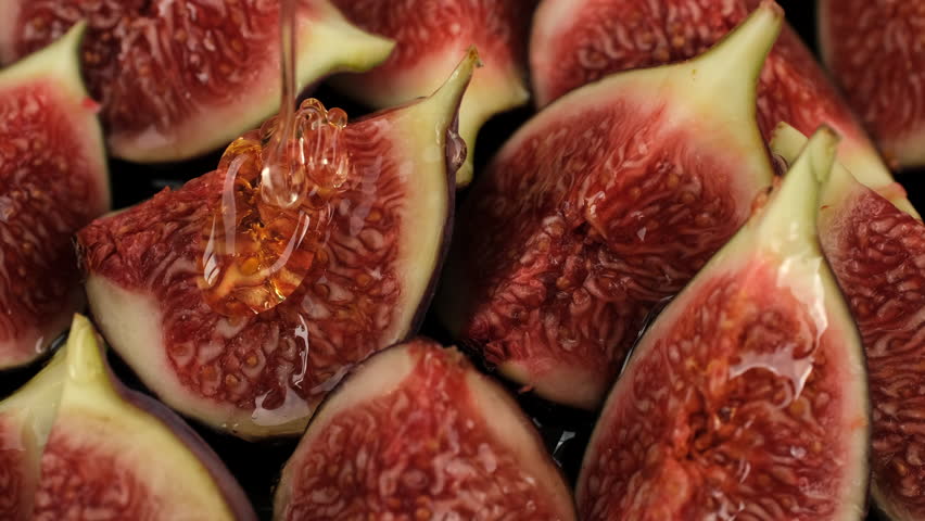 Honey pouring on figs slices, close up. Healthy breakfast, natural dessert, vegetarian food