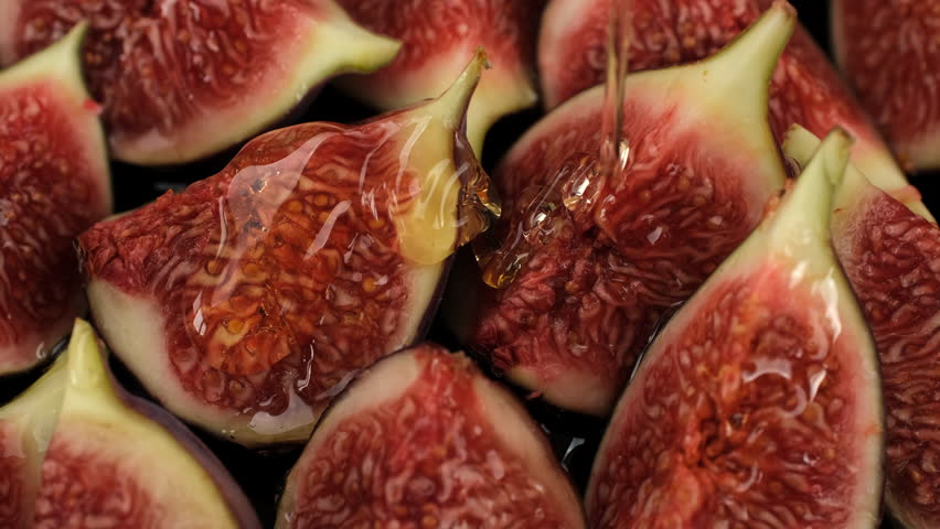 Honey pouring on figs slices, close up. Healthy breakfast, natural dessert, vegetarian food