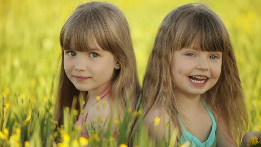 Two girls sitting in  flowers and smiling
