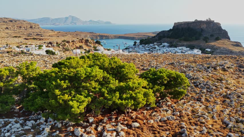 This captivating aerial view captures the rugged coastline of Rhodes, Greece, revealing a picturesque scene of the sea, hills, and ancient ruins bathed in sunlight.