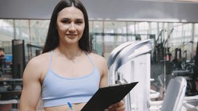 Fitness trainer guiding clients in a gym setting while holding a clipboard and smiling confidently - Powered by Shutterstock - Get 15% off with code: PIKWIZARD15