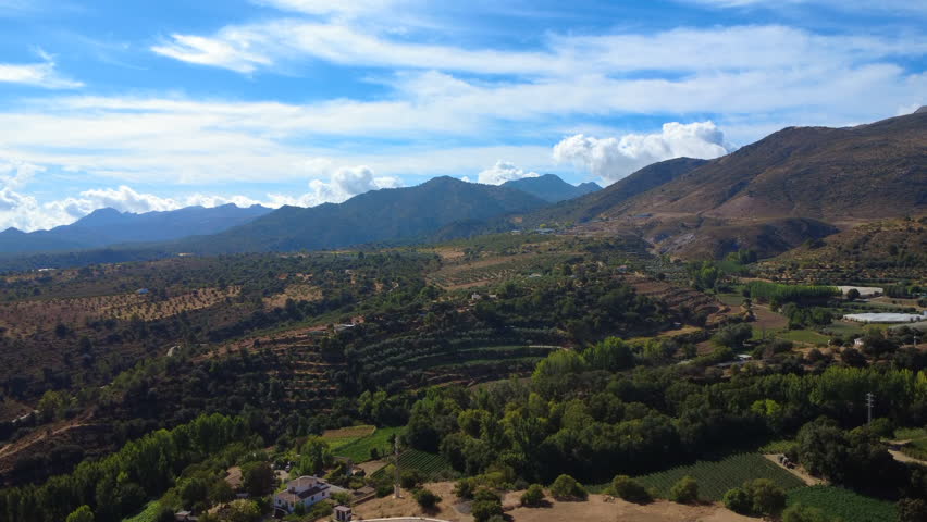 4K aerial video of the countryside near Játar in the Sierra Nevada, showing rolling hills, farmland, and green valleys under clear sunny skies in rural Andalusia.